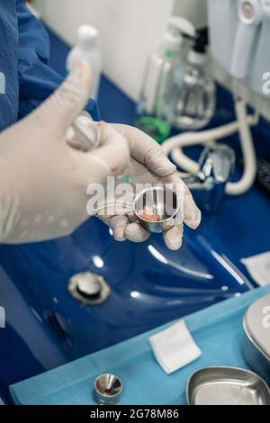 Unrecognized dentist wearing protective clothes and latex gloves holding a extraction from a patient. Stock Photo