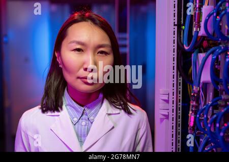 Portrait of confident skilled young Asian server engineer in white coat standing near cables in cabinet Stock Photo