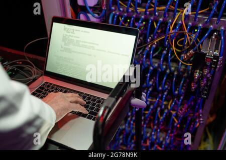 Close-up of unrecognizable technician standing at cart against server cabinet and setting up server using laptop Stock Photo