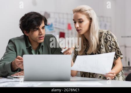 couple of young designers pointing at laptop while working in fashion atelier Stock Photo