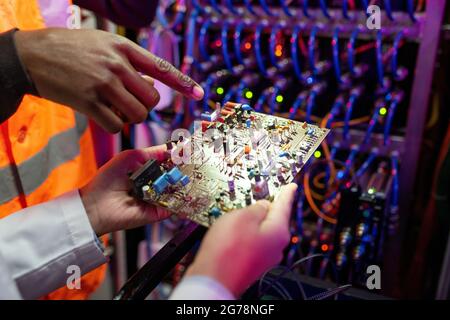 Close-up of black engineer pointing at computer circuit board while discussing its structure with colleague Stock Photo