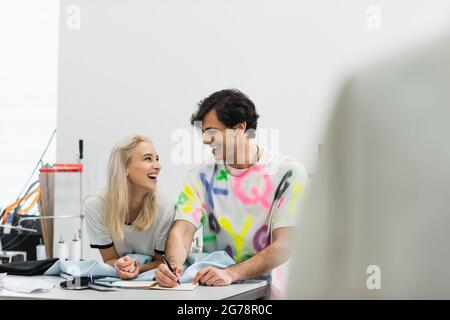 cheerful designers talking in atelier near samples of cloth and colors, blurred foreground Stock Photo
