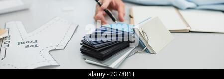 cropped view of blurred designer with pen near color samples and sewing pattern, banner Stock Photo