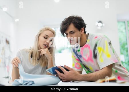 couple of young fashion designers choosing color from palette in tailor shop Stock Photo