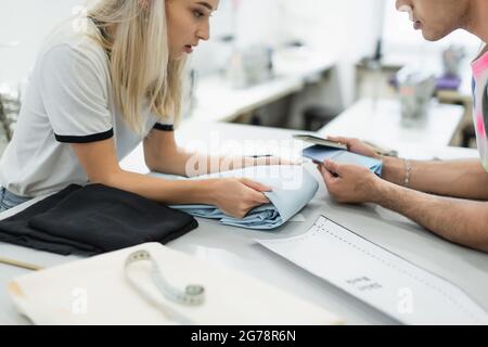 cropped view of designers looking at tissue and color palette near sewing pattern, blurred foreground Stock Photo