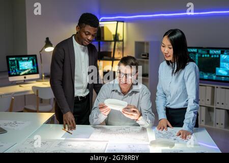 Team of Positive multi-ethnic automobile designers working with blueprint and discussing new model of car Stock Photo