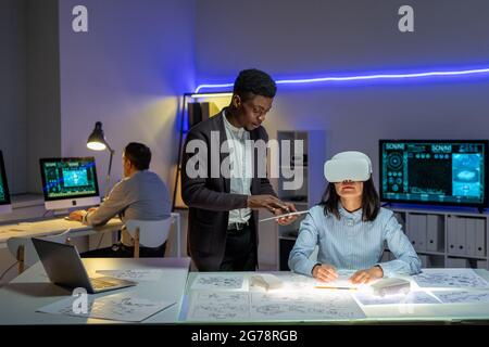 Young African-American man using tablet while managing virtual reality of colleague while she designing automobile Stock Photo