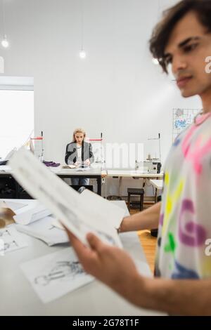 blurred fashion designer looking at drawing near colleague working on background Stock Photo