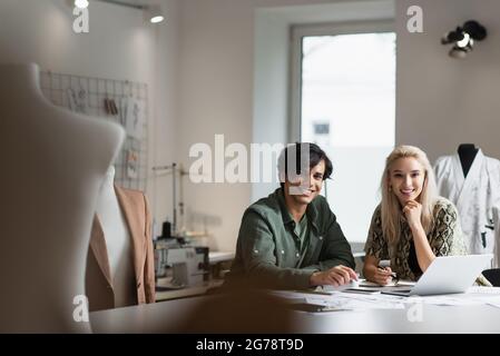happy designers smiling at camera while working in fashion workshop on blurred foreground Stock Photo