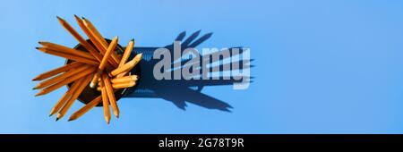 Graphite pencils in a metal grid-container on the office table top view on blue background. Stock Photo