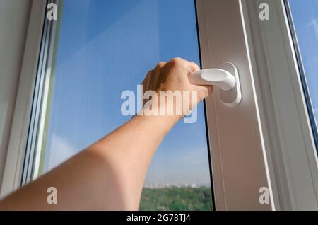 Woman's hand opens the handle of a plastic window against a blue sky Stock Photo