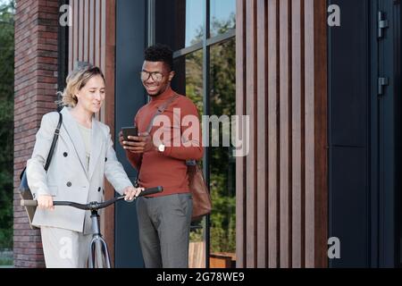 Small group of intercultural colleagues with smartphone having outdoor meeting Stock Photo