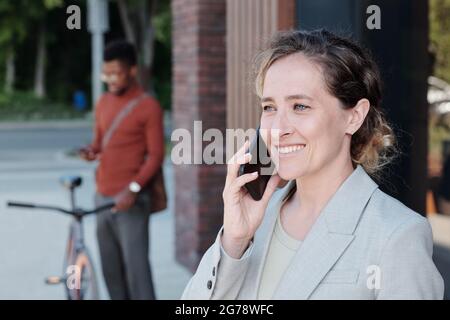 Young businesswoman in elegant suit talking to colleague or friend on mobile phone Stock Photo