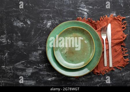 Empty green plate served with knife, fork and table napkin. Mockup template plate for luxury dinner with copy space on dark black concrete table top Stock Photo
