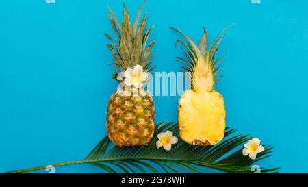 Pineapples whole tropical summer pineapples fruits and sliced pineapple halves with tropical plumeria flowers composition on blue color summer Stock Photo