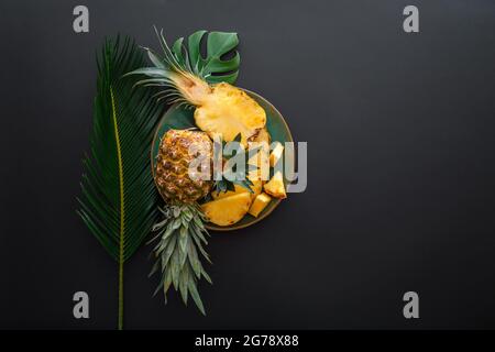 Sliced Pineapple on plate with tropical palm leaves. Bromelain whole pineapple summer fruit halves pineapple on black dark background. Summer fruit Stock Photo