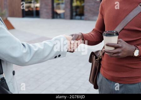 Businessman with drink shaking hand of female in suit after making agreement Stock Photo