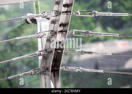 A close up view of tension steel cables with steel fasteners, a detail of frame on glass bridge with fastening engineering construction stainless stee Stock Photo