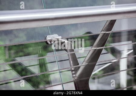 railings with glass panels fastenings enclosing the edge of the pedestrian bridge with tension steel cables for tensioning the structure close-up. Stock Photo