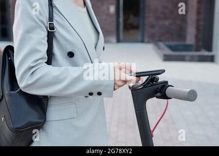 Contemporary businesswoman with smartphone using mobile application to rent scooter Stock Photo