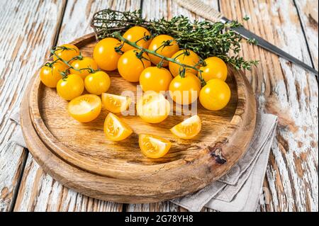 Sliced yellow cherry tomato on a wooden tray with herbs. White wooden background. Top view Stock Photo