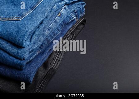 Stack of blue jeans on black background with copy space. Frame made of blue jeans trousers stack. Stock Photo