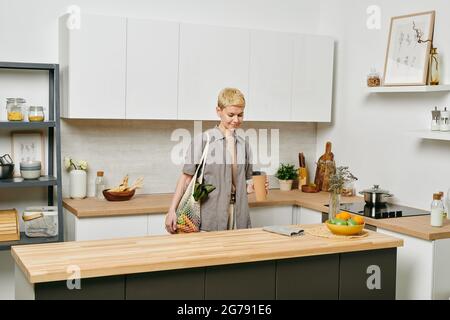 Young female with drink standing by wooden kitchen table Stock Photo