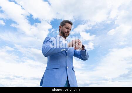 handsome mature man businessman in suit check time on wristwatch on sky background, punctuality. Stock Photo