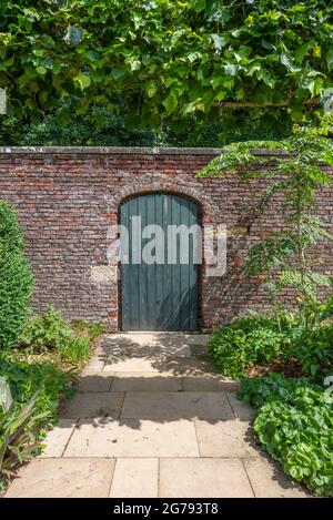A green walled garden door in a red brick wall with a slabed footpath Stock Photo