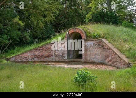 Old ice house burried under a grass mound with red bricks and open gate. Stock Photo