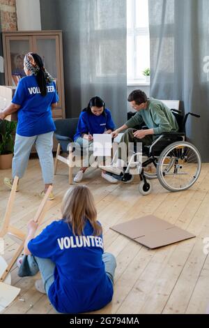 Group of female volunteers working in apartment of young disabled man Stock Photo