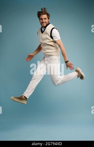 Full length portrait of an excited young man in white t-shirt jumping while celebrating success isolated over blue background Stock Photo