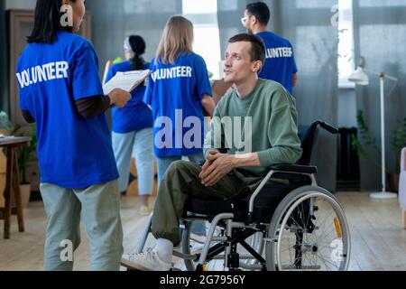 Disabled man in wheelchair talking to Asian female volunteer Stock Photo