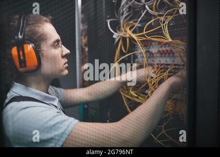 Side view of young network engineer connecting cables in server room during maintenance work in data center, copy space Stock Photo