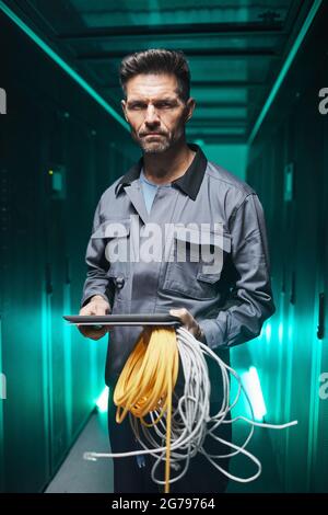 Vertical portrait of mature network engineer using digital tablet in server room during maintenance work in data center Stock Photo