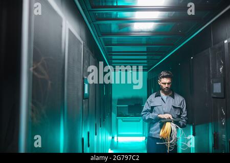 Wide angle portrait of mature network engineer using digital tablet in server room during maintenance work in data center, copy space Stock Photo
