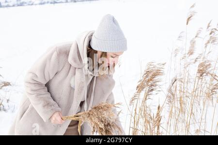 A young woman in a beige dress of neutral colors collects pampas grass.  Stock Photo