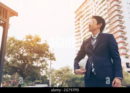 engineer holding white helmet for workers security on background of new highrise apartment buildings.Construction workers working for architectural pr Stock Photo
