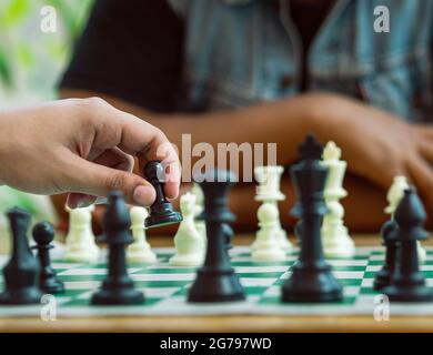 Chess game on a green board, a hand holds a black pawn Stock Photo