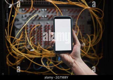 Close up of network engineer holding smartphone with blank screen in server room during maintenance work in data center, copy space Stock Photo