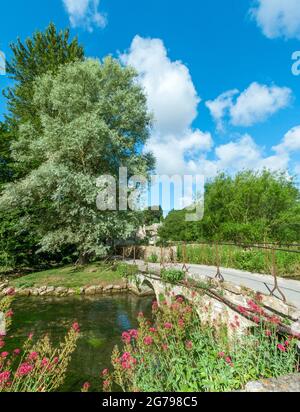 Great Britain, GL Gloucestershire, Bibury near Cirencester, bridge over the River Coln, historic stone bridge, footpath to Arlington Row. The artist and writer William Morris called Bibury 'the most beautiful village in England'. Stock Photo