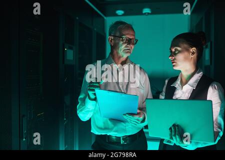 Futuristic waist up portrait of two data scientists using laptop in server room while working with supercomputer, copy space Stock Photo