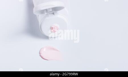Squeezed cream tube with pink moisturizer smear on white. Cleansing mask for beauty SPA. Skin care product promo banner with space for text copy Stock Photo