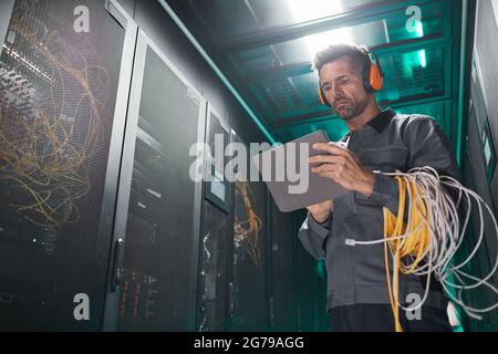 Low angle portrait of network engineer using tablet in server room during maintenance work in data center, copy space Stock Photo