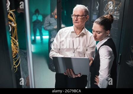 High angle view at two data scientists using laptop while working with supercomputer in data center, copy space Stock Photo