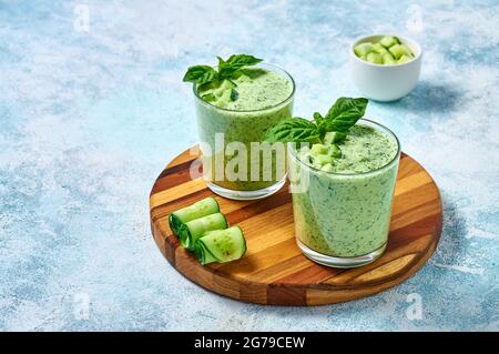 Cucumber Gazpacho - cold summer soup with basil in glasses on wooden board on light background. Stock Photo