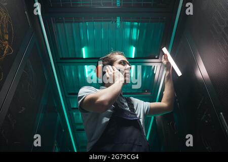 Low angle portrait of male network engineer speaking by smartphone in server room while working in data center, copy space Stock Photo