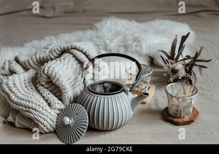 Close-up of teapot in scandinavian style with tea with knitted element and decor details. Stock Photo