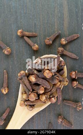 Top View of Dried Cloves on Wooden Spoon with Some Scattered on the Background Stock Photo