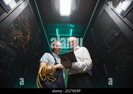 Low angle portrait of two engineers using tablet in server room while doing maintenance work in data center, copy space Stock Photo